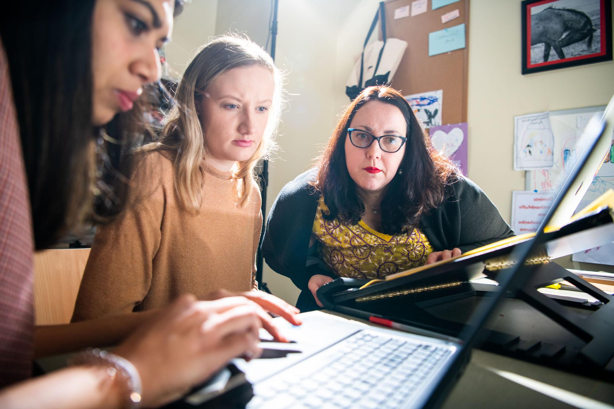 A professor watches intently as students complete work on a laptop computer